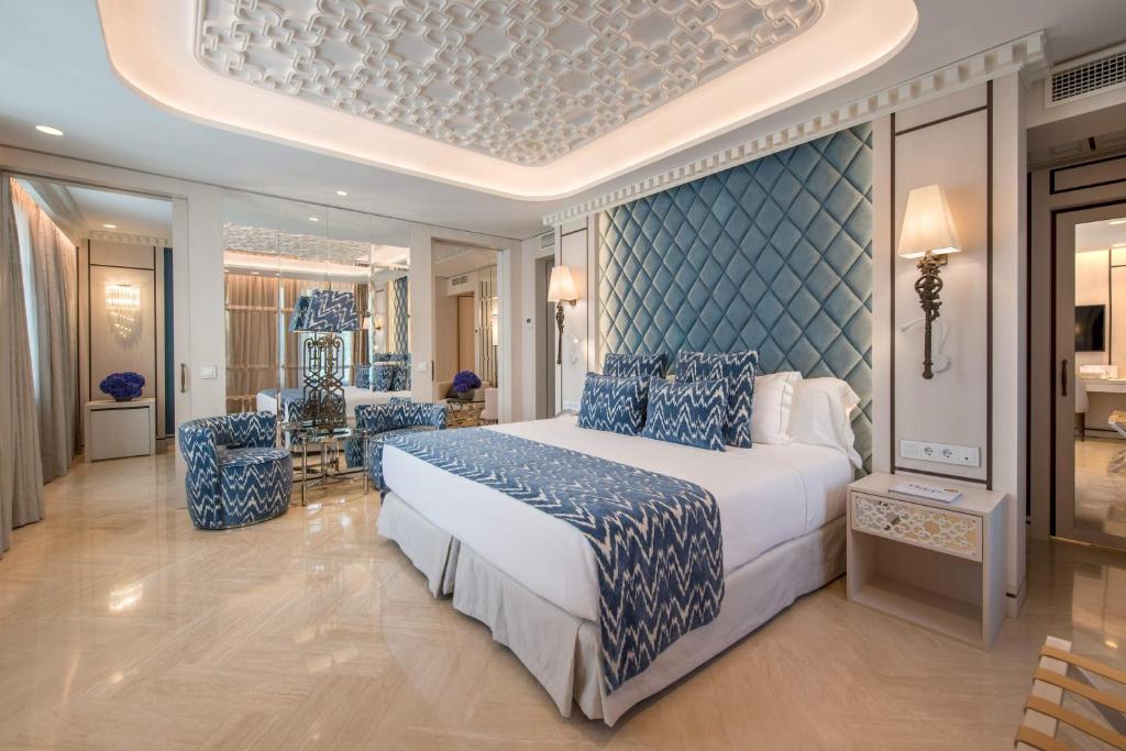 Elegants viesnīcas numurs ar mūsdienīgu interjeru, kurā ir gultas ar zilu apdari, dekoratīvi spilveni un stilīgas mēbeles. Sienas rotā spoguļi un mūsdienīgas lampas, radot siltu un viesmīlīgu atmosfēru.