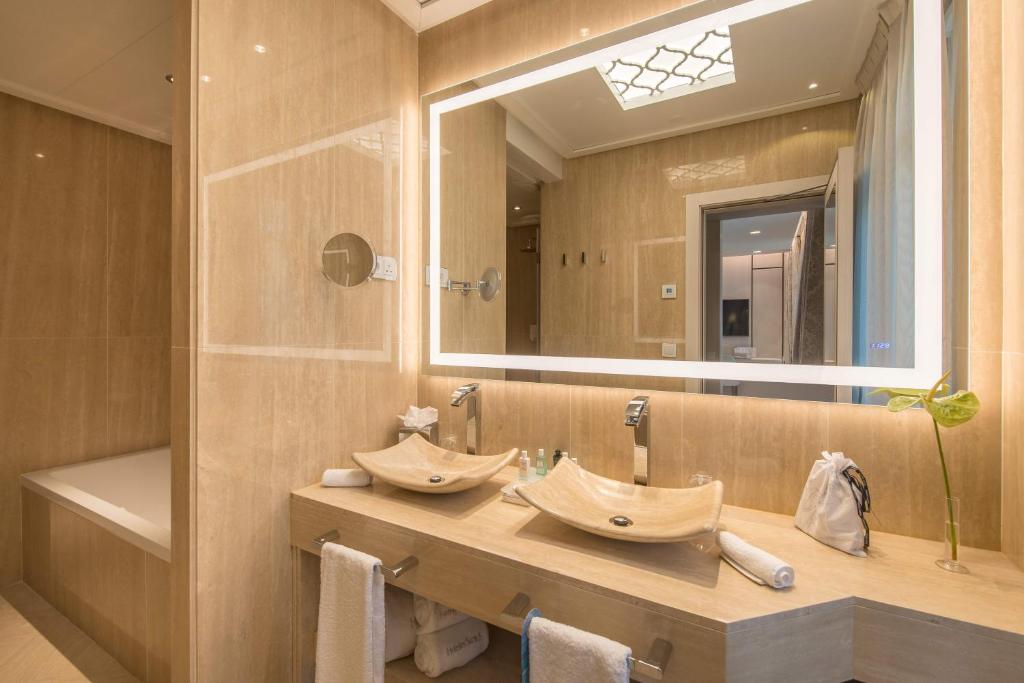 Mūsdienīga vannas istaba ar akmens izskata izlietni, spoguli ar apgaismojumu un elegantu interjeru. Vannas istaba ir gaiša un plaša, radot relaksējošu atmosfēru.