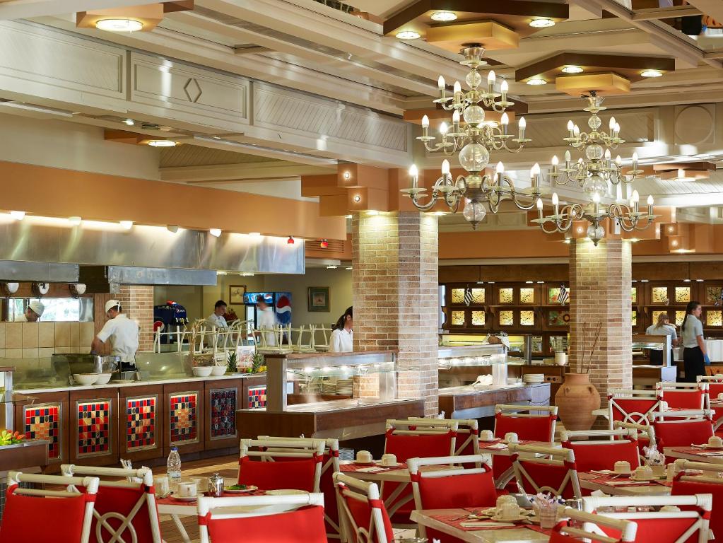 Restorāns Knossos Royal ar elegantiem galdiem un šefpavāriem, kas gatavo maltītes.