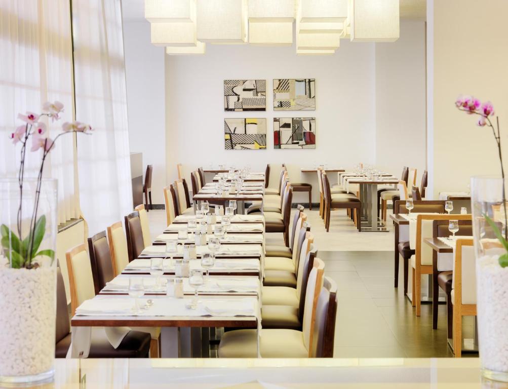 Mūsdienīgs restorāns ar elegantiem galdiem un krēsliem, apgaismots ar stilīgām lustrajām lampām un dekorēts ar abstraktām gleznām uz sienas. Plāns un gaišs interjers rada patīkamu atmosfēru.