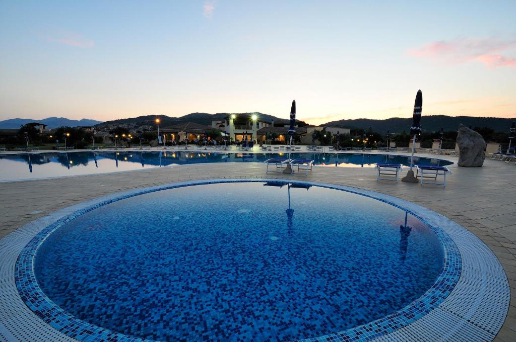 Viesnīcas Baia del Porto baseins ar skatu uz kalniem saulrietā.