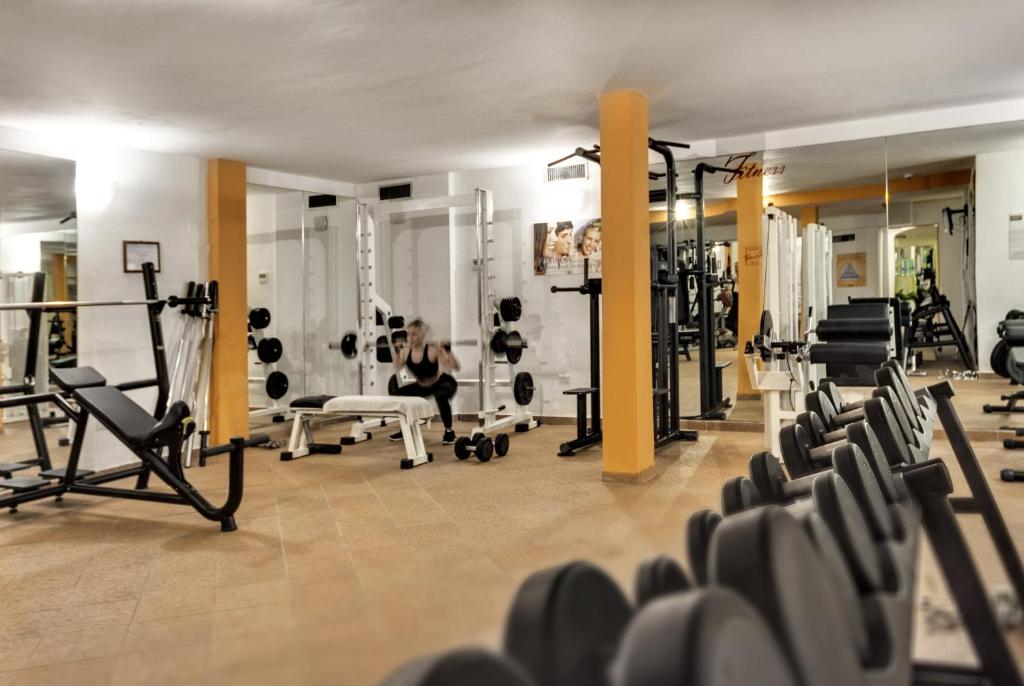 Fitnessa zāle ar dažādām treniņu iekārtām un svariem, kur cilvēks veic vingrinājumus. Iekārta un aprīkojums ir labi organizēti, radot motivējošu vidi treniņiem.