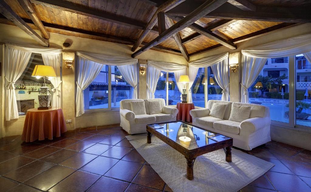 Lieliska viesistaba ar divām baltām dīvāniem, koka griestiem un lieliem logiem, kas paver skatu uz baseinu. Telpa ir apgaismota ar siltu gaismu un dekorēta ar elegantiem elementiem.