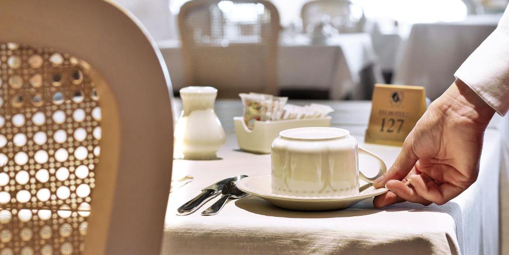 Baltas kafijas krūze tiek pasniegta viesnīcas restorānā, blakus ir saldumi un krējums. Galda uzstādījums ir elegants un viesmīlīgs.