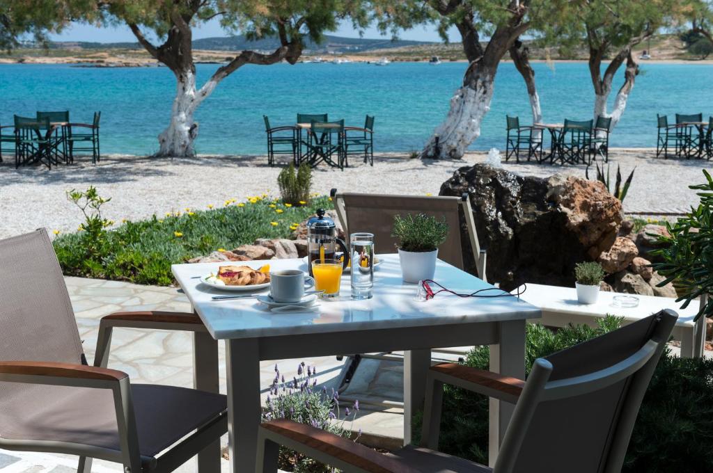 Lieliska brokastu aina pie jūras ar galdu, kas klāts ar kafiju, sulu un maizēm, un fona ir mierīga pludmale ar kokiem un krēsliem.