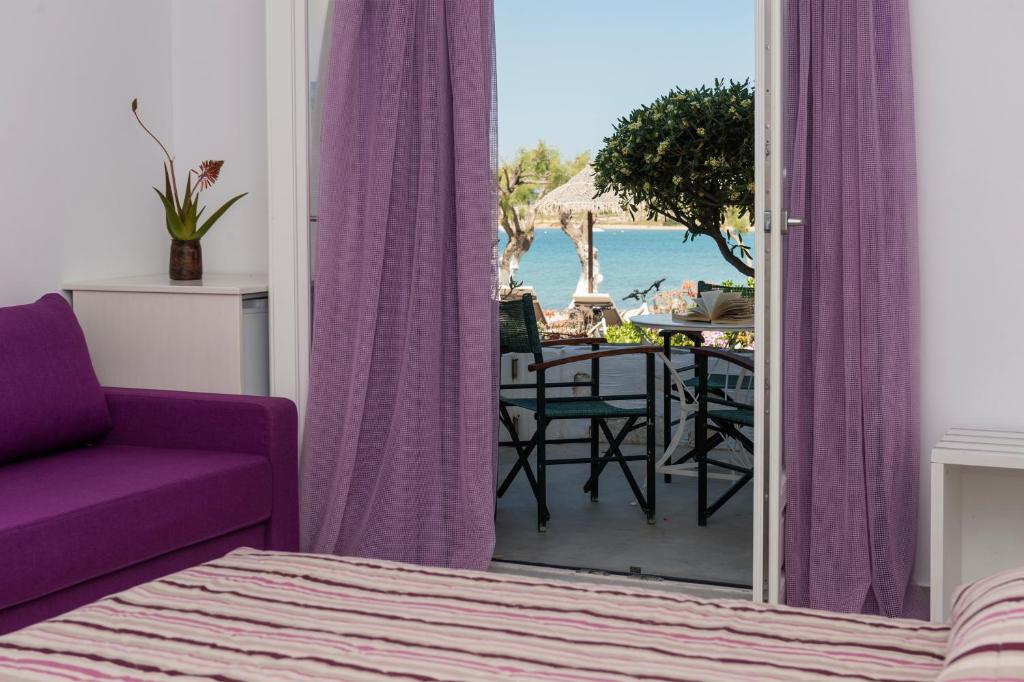 Skats no istabas uz terasi ar skatu uz jūru, izceļot purpursarkano dīvānu un ziedu dekoru.