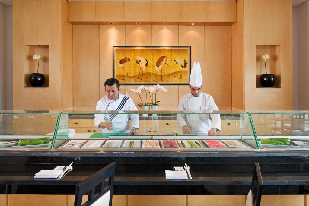 Sushi gatavošanas process diviem pavāriem, kas strādā pie sushi bāra ar dažādiem sastāvdaļām un estētisku interjeru.