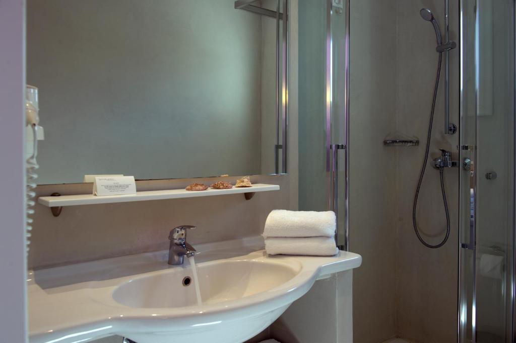 Mūsdienīgs un elegants vannas istabas interjers ar dušu, izsmalcinātu izskatu un tīras, baltas dvieļus. Uz plaukta ir sīkumi, piešķirot telpai mājīgu sajūtu.