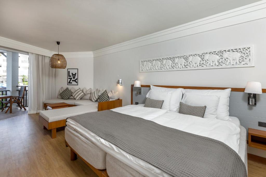 Mūsdienīga viesnīcas numura interjers ar ērtu gultu, dīvānu un dekoratīviem elementiem. Telpa ir gaiša un labi iekārtota, nodrošinot relaksējošu atmosfēru.