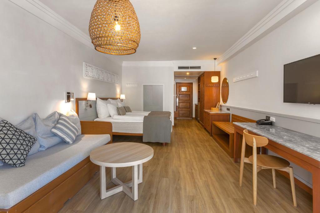 Gaiša un moderna viesnīcas istaba ar divām gultām, dīvānu un koka mēbelēm. Telpa ir apgaismota ar stilīgu lampu, radot mājīgu atmosfēru.