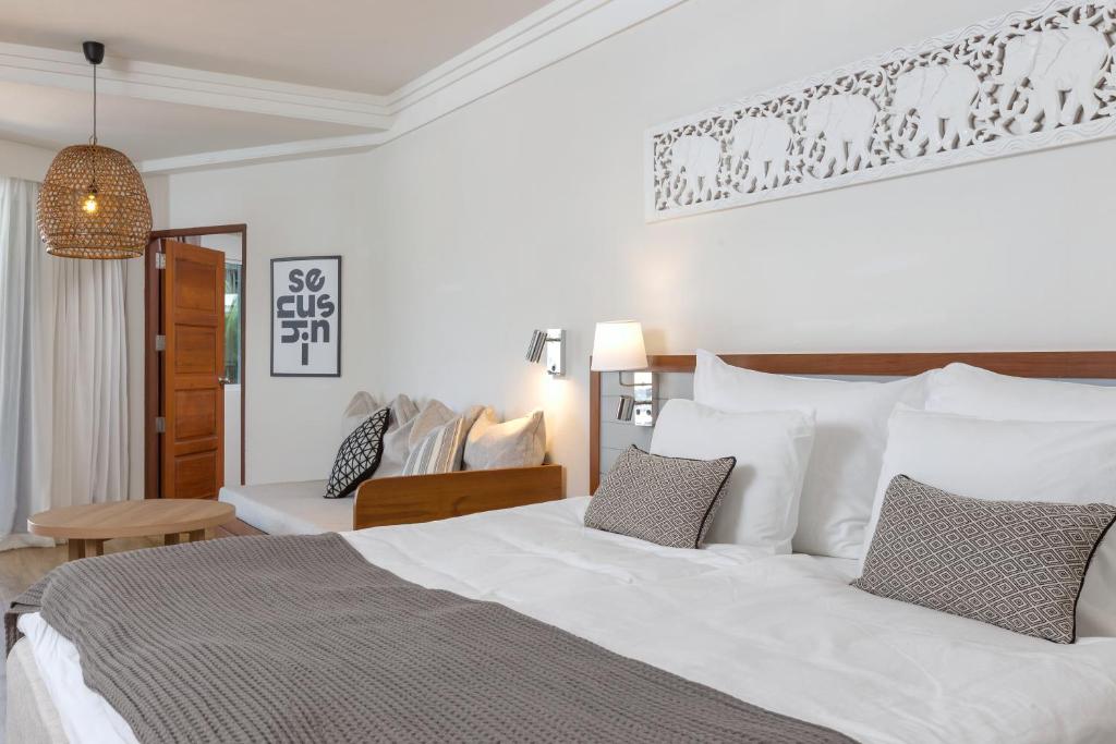 Mūsdienīga guļamistaba ar divguļamo gultu, dekoratīviem spilveniem un stilīgu apgaismojumu. Interjerā ir redzams ērts dīvāns un mākslinieciska sienu apdare.