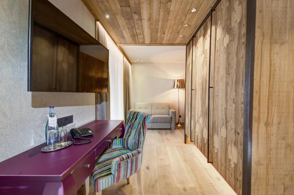 Mūsdienīgs viesnīcas numurs ar koka grīdu, krāsainu krēslu pie rakstāmgalda un televizoru pie sienas. Numurā ir dabiska gaisma un eleganta dekorācija.