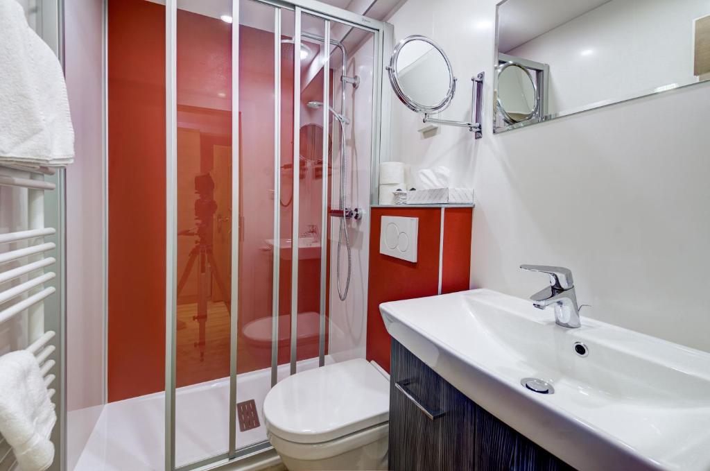 Mūsdienīga vannas istaba ar dušas kabīni, izlietni un tualeti, sarkanas un baltas krāsas akcentiem. Telpa ir labi apgaismota un iekārtota ar higiēnas piederumiem.