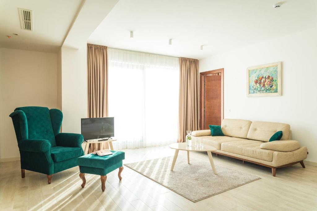 Mūsdienīga viesistaba ar gaišiem toņiem, ērtiem dīvāniem un izteiksmīgu zaļu krēslu, kas piešķir telpai stilīgu akcentu. Logi ar caurspīdīgām aizkariem ļauj plūst dabīgai gaismai.