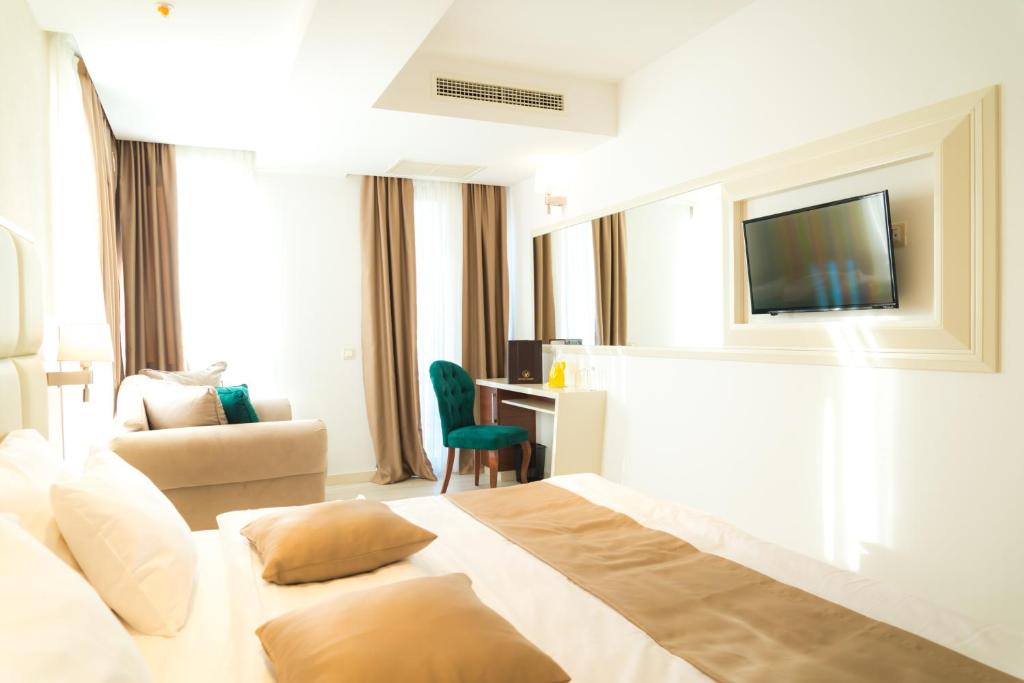 Mūsdienīga viesnīcas numura interjers ar gaisīgu dizainu, ērtiem krēsliem un televizoru. Logi nodrošina dabisko apgaismojumu, radot mājīgu atmosfēru.