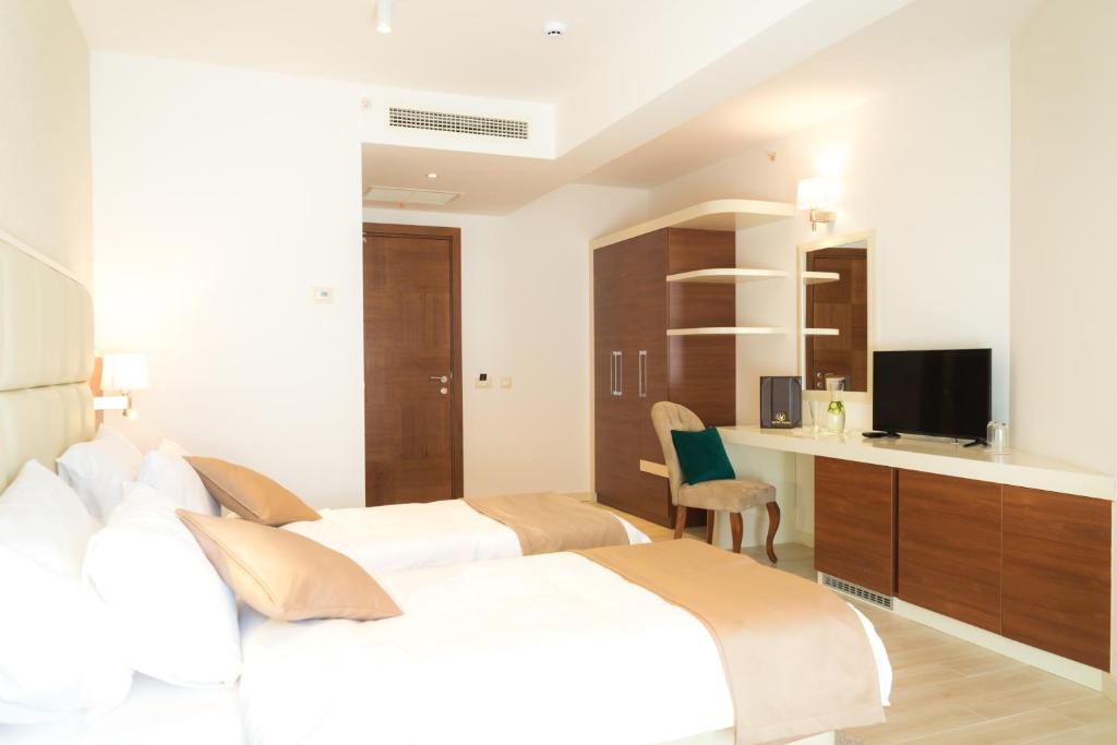 Gaisma un mūsdienīga guļamistaba ar diviem gultām, televizoru un elegantu mēbeļu komplektu. Telpā ir arī darba zona un skapji, radot komfortablu un funkcionālu vidi.