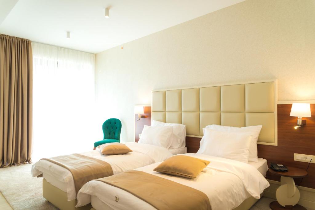 Mūsdienīgs viesnīcas numurs ar divām gultām, zaļo krēslu un dabisku apgaismojumu. Ideāls komfortablas atpūtas nodrošināšanai.