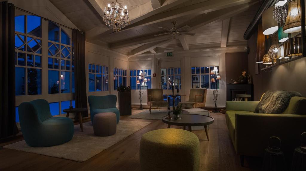 Elegantā viesistaba ar modernām mēbelēm, kas apgaismota ar siltu gaismu, radot mājīgu atmosfēru. Lielie logi un grezna lustrā piešķir telpai unikālu šarmu.