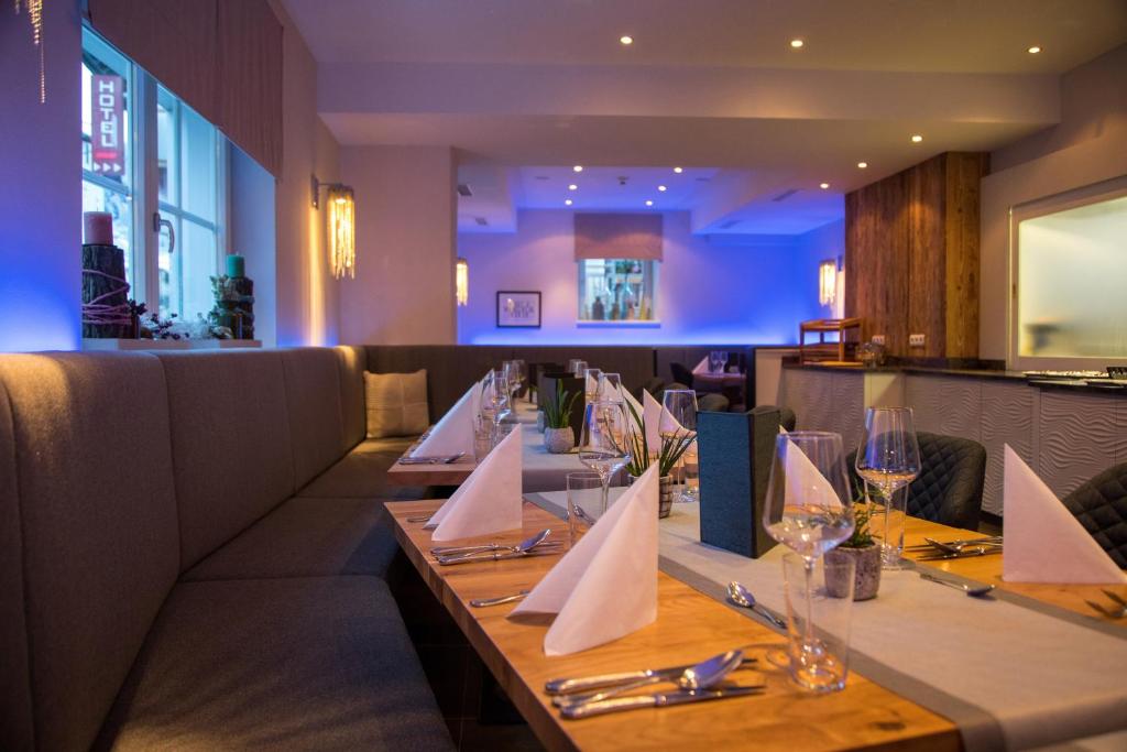 Elegants restorāns ar mūsdienīgu interjeru, kas iekārtots ar gaišām krāsām un patīkamu apgaismojumu. Galdi ir sakārtoti ar elegantām galdautām un traukiem, gatavi viesu uzņemšanai.