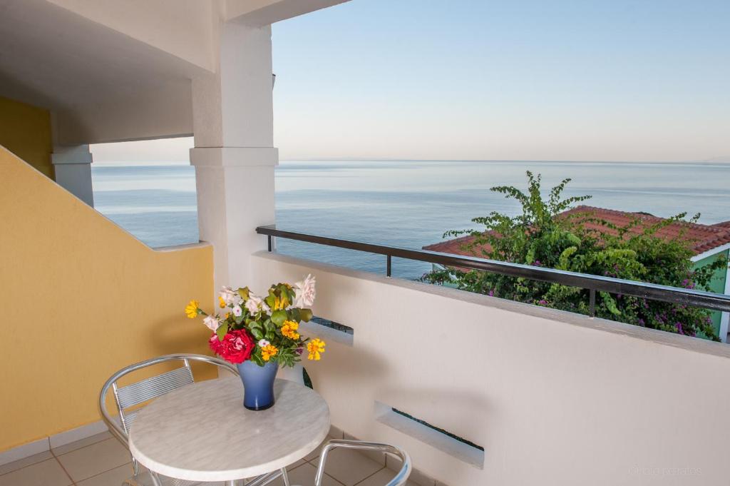Balkons ar skatu uz jūru, uz galda novietots ziedu pušķis un metāla krēsli. Apspēlēts mierīgs un relaksējošs atmosfēra.