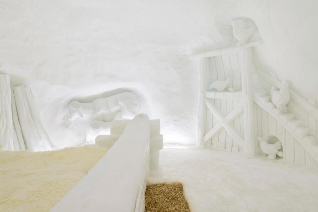 Sniega viesnīcas interjers ar izsmalcinātām sniega skulptūrām, tostarp guļamistaba un lauku ainavas elementi.