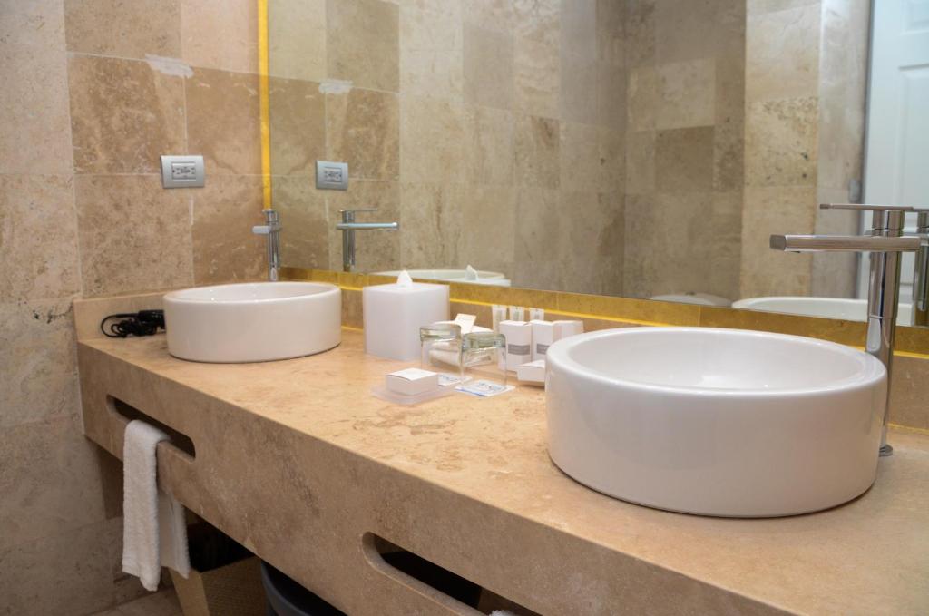 Moderns vannas istabas dizains ar diviem baltajiem izlietnēm, dabīgā akmens virsmu un higiēnas piederumiem. Svaiga un eleganta atmosfēra ar minimālisma elementiem.