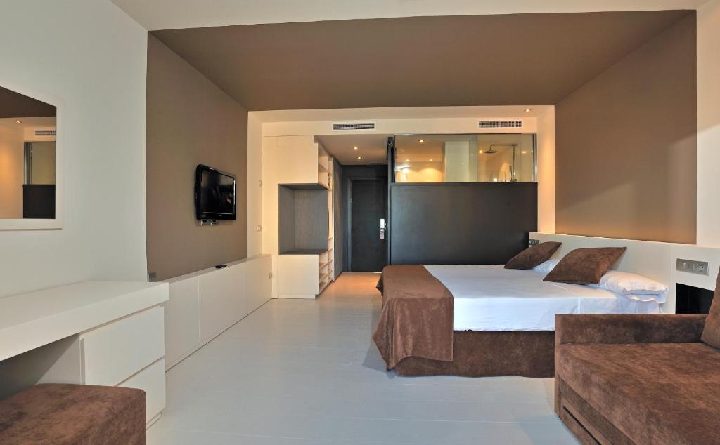 Mūsdienīga viesnīcas numura interjers ar divvietīgu gultu, brūniem gultas piederumiem un dīvānu, kā arī TV un rakstāmgaldu. Telpa ir gaiša un plaša, ar neitrālām krāsām.