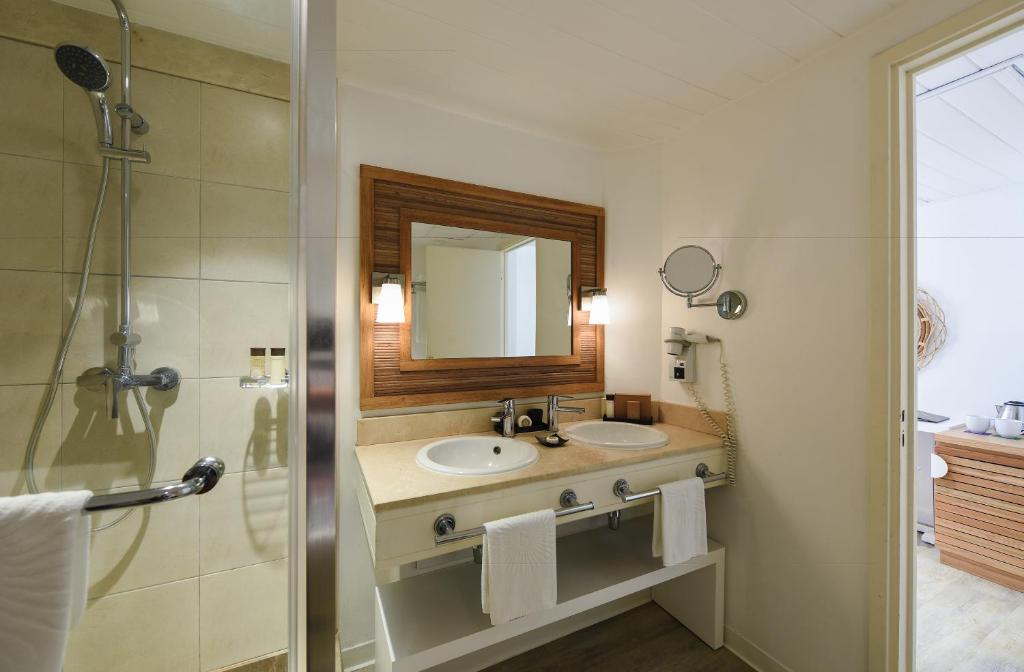 Mūsdienīgs vannas istabas interjers ar diviem izlietnēm, spoguli un dušas kabīni, kas nodrošina komfortu un stilu. Gaišas krāsas un koka akcenti rada patīkamu atmosfēru.