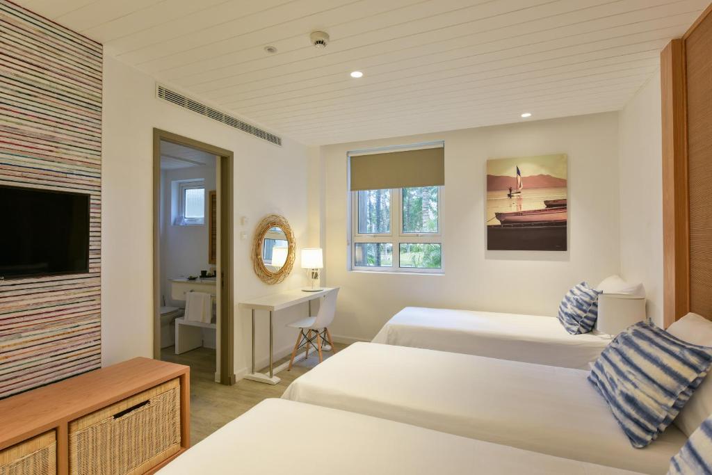 Mūsdienīga viesnīcas istaba ar divām gultām, darba galdu un televizoru, kas izvietota gaišā interjerā ar dabas skatu. Uz sienas ir gleznas un stilīga apgaismojuma lampiņa.