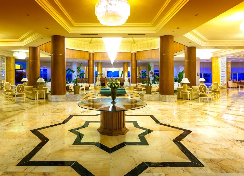 Elegants viesnīcas vestibils ar marmora grīdu un modernu interjeru, ieskaitot zaļus augus un komfortablas sēdvietas. Gaismas elementi rada siltu atmosfēru.