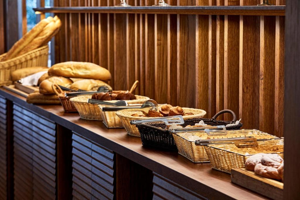 Bagātīgs maizes un konditorejas izstrādājumu bufete ar dažādām maizes šķirnēm un groziem, kas sakārtoti pie koka plauktiem.