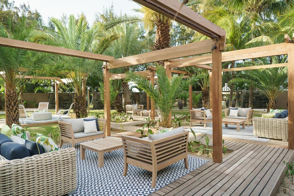 Mūsdienīga āra atpūtas zona ar koka mēbelēm, palmām un dekoratīviem spilveniem, radot relaksējošu atmosfēru. Ideāla vieta, kur baudīt dabu un atpūtu.