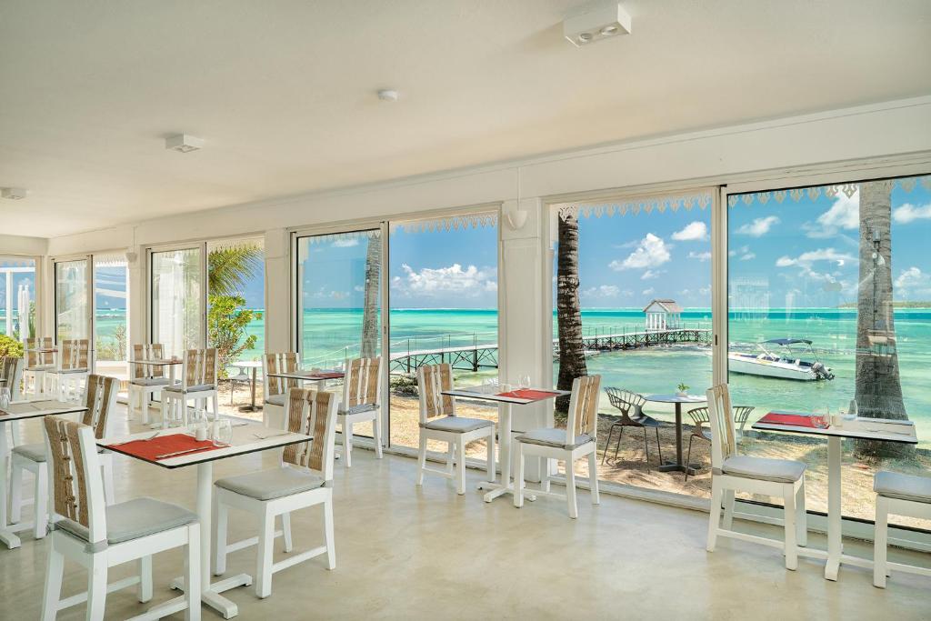 Gaiša restorāna iekārtojums ar skatu uz tirkīza jūru un piestātni, kurā redzami balti galdi un krēsli. Ideāla atmosfēra relaksācijai un baudīšanai.