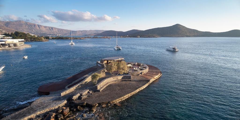 Skats uz gleznainu jūras piekrasti ar maziem kuģiem un kalnu ainavām, radot mierīgu un relaksējošu atmosfēru. Ideāla vieta atpūtai pie ūdens.