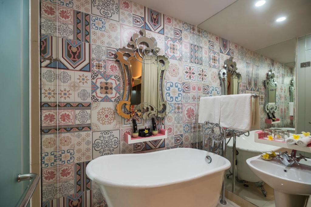 Vannas istaba ar stilīgu flīžu sienu, brīvu vannu un spoguļiem, kas piešķir telpai elegantu izskatu. Svaigi ziedi un vannas piederumi papildina atmosfēru.