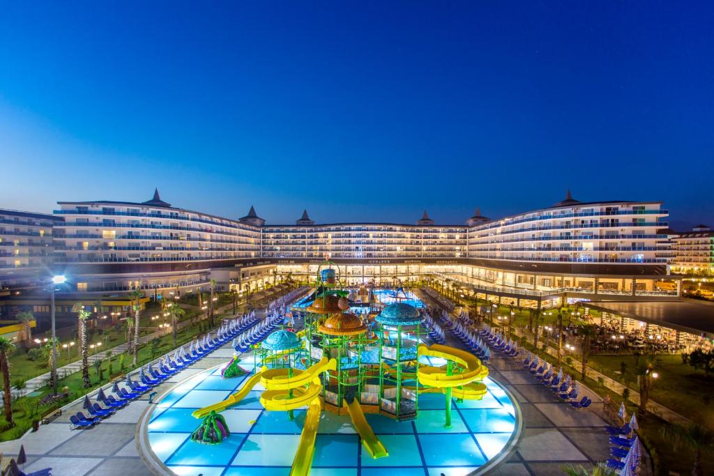 Lielisks kūrorts ar ūdens slidkalniņiem un peldbaseinu, apgaismots tumsā, radot atpūtas atmosfēru. Apkārt esošās saulessargu rindas un viesnīcas ēka piešķir ainavai elegantu izskatu.