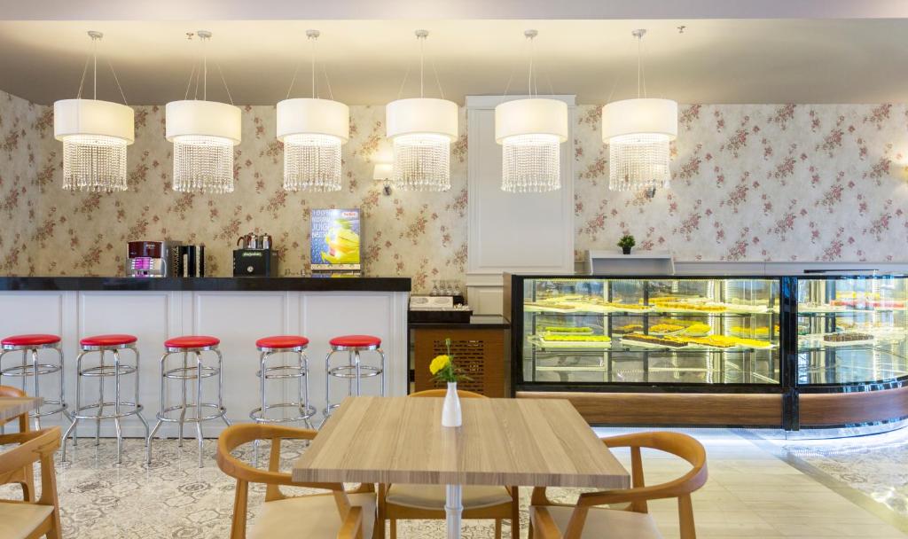 Moderns kafijas veikals ar elegantiem piekariņiem un ziedu tapetēm, kas piedāvā saldumus vitrīnā un sarkanas krēsla malas pie bāra letes.