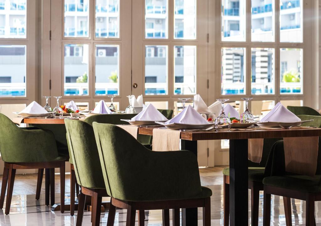 Elegantā restorāna interjers ar zaļām krēslām un galdiem, pie kuriem ir sakārtoti galdauti un galda piederumi. Labi apgaismots, ar lieliem logiem, kas ļauj iekļūt dabiskai gaismai.