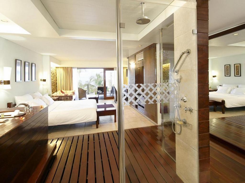 Mūsdienīgs viesnīcas numurs ar atklātu dušas zonu un elegantu interjeru, kas ietver lielu gultu un atpūtas stūrīti. Gaismas un koka elementi rada patīkamu atmosfēru.