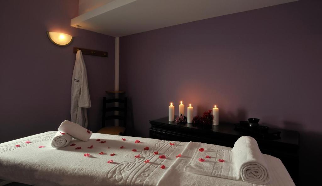 Mierīga masāžas telpa ar purpura sienām, uz galda izvietoti dvieļi un rožu ziedlapiņas, apgaismojums no svečiem. Ideāla atmosfēra relaksācijai.