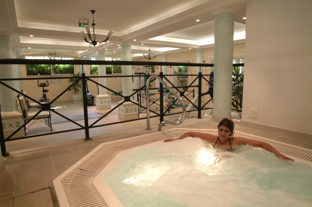 Spa centrā relaksējoša burbuļvanna ar sievieti, kas izbauda ūdens procedūras. Moderns interjers ar zaļām augu dekorācijām un sporta aprīkojumu.