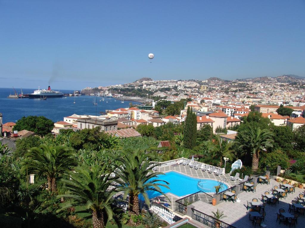 Skats uz piejūras pilsētu ar kuģiem un debesīm, kas ir skaidras. Peldbaseins un tropu augi pie viesnīcas dārza.