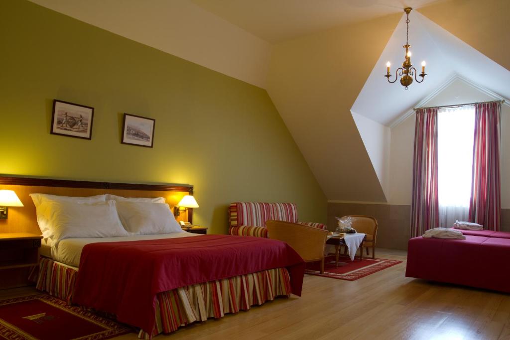 Mūsdienīgs viesnīcas numurs ar zaļu sienu, divām gultām un omulīgu atpūtas stūrīti. Logā plūst dabiska gaisma, radot komfortablu atmosfēru.