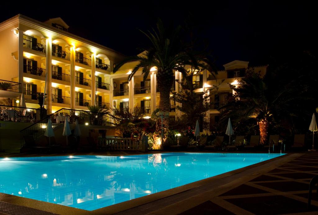 Nakts ainava ar apgaismotu viesnīcu un baseinu, kas atspoguļo koku un apgaismojumu.