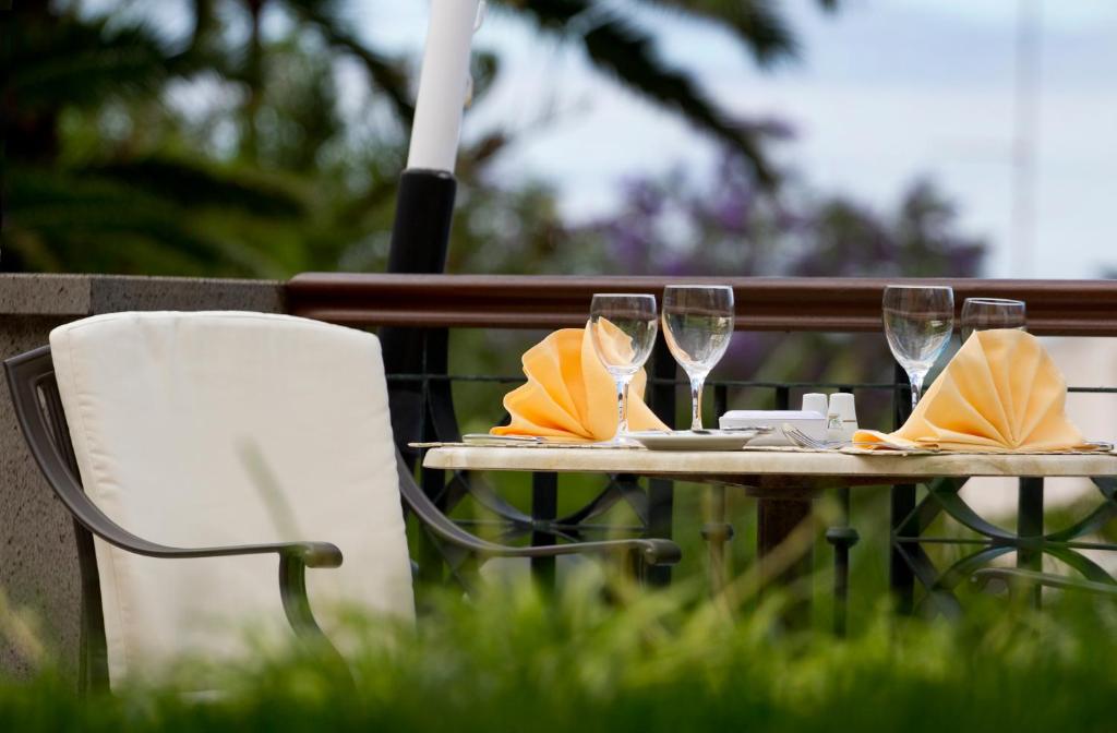 Romantisks galdiņš ar oranžiem salvešu salocījumiem un glāzēm, izvietots dārzā, ko ieskauj zaļumi. Ideāls iestatījums vakariņām ārpus telpām.