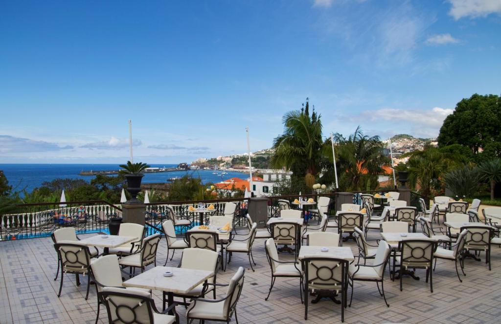 Aizraujoša terase ar skatu uz jūru, kurā redzamas tukšas galdi un krēsli, apzaļumotas zonas un kalnainas ainavas. Ideāli piemērota atpūtai un ēdienreizes baudīšanai brīvā dabā.