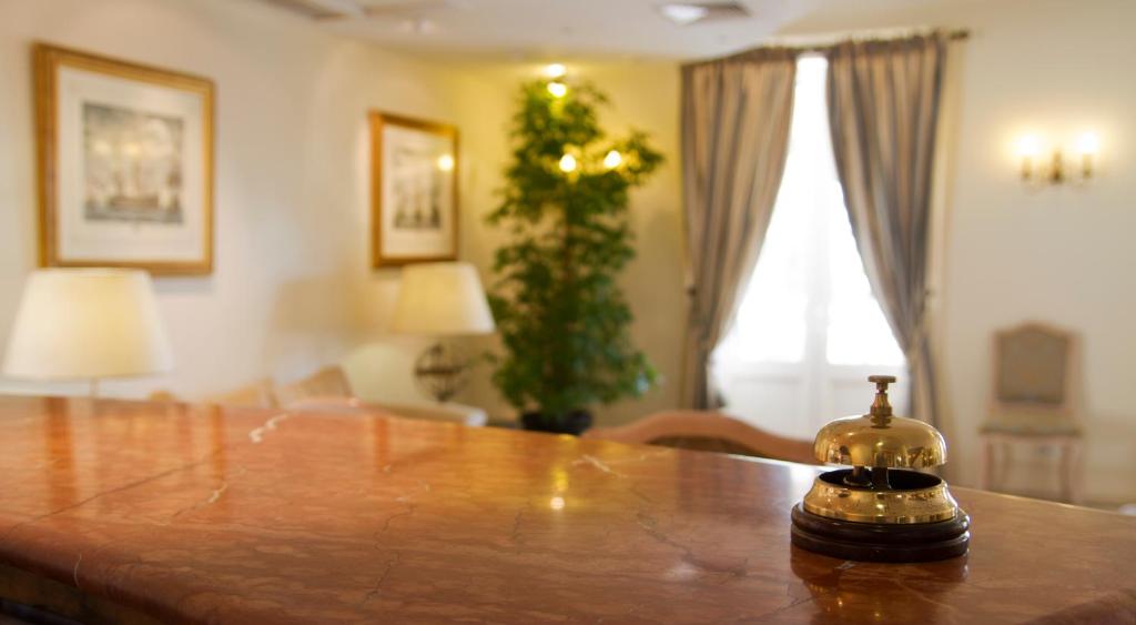 Elegants viesnīcas reģistratūras galds ar zeltītu zvanu, apgaismotām lampām un dekoratīvām gleznām uz sienām, radot viesmīlīgu atmosfēru.