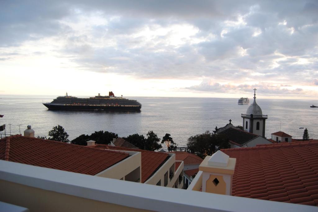 Kuģis peld pa mierīgu jūru, fonā redzamas debesu krāsas un vēsturiska baznīca. Skats uz krastmalu un apkārtējo ainavu rada relaksējošu atmosfēru.