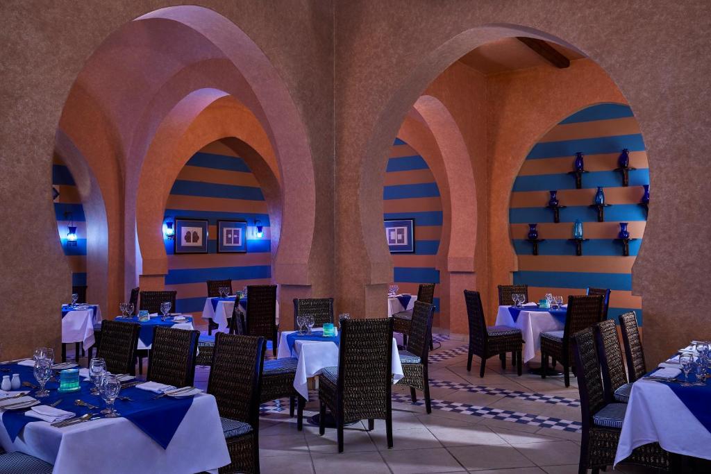 Elegantā restorāna interjers ar zilām un brūnām svītrām, ar arku formas nišām un romantisku apgaismojumu. Galdi ir sakārtoti ar baltām un zilu galdautu, radot patīkamu atmosfēru.