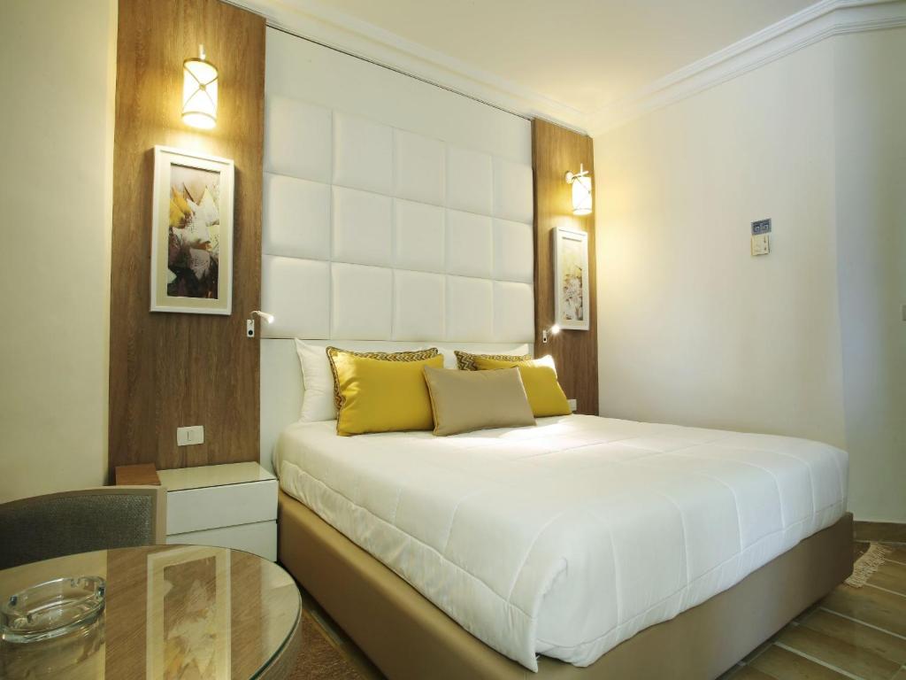 Mūsdienīgs viesnīcas numurs ar divguļamo gultu un siltām dzeltenām spilveniem, apgaismots ar gaismas ķermeņiem un dekorēts ar mākslas darbiem uz sienām.